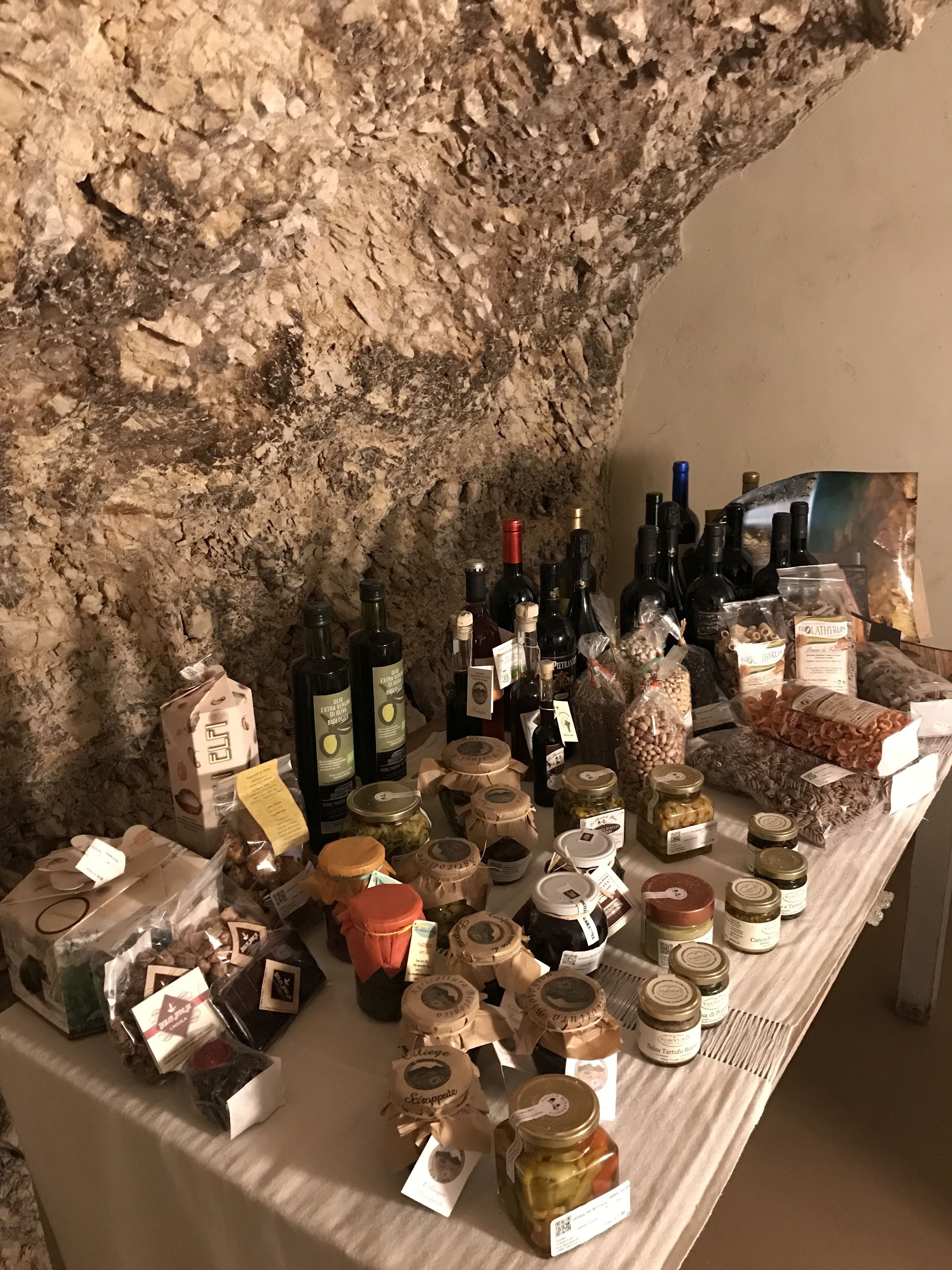 A table with various food items and bottles, possibly for sale, against a textured wall.