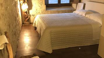 A cozy bedroom with a wooden bed, a chair, a nightstand, and a window with a view.