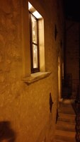 Un estrecho pasillo de piedra con una pequeña ventana y una puerta de madera.