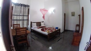 A bedroom with a bed, a wooden chair, a small table, and a window with curtains.