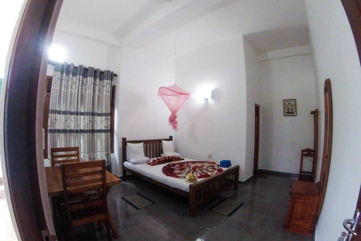 Une chambre à coucher avec un lit, une chaise en bois, une petite table et une fenêtre avec des rideaux.