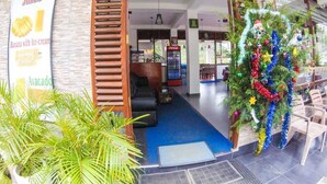 A hotel lobby with a blue carpet, wooden shutters, a Coca-Cola refrigerator, and a Christmas tree.