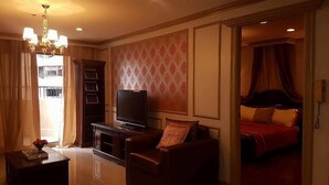 A hotel room with a television, a sofa, a bed with red bedding, a chandelier, and a patterned wallpaper. - Elegant 2BRCondo in the Heart of Ortigas (Pasig)