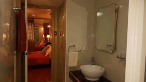 A hotel room with a bed, a bathroom with a sink and mirror, and a door leading to another room. - Elegant 2BRCondo in the Heart of Ortigas (Pasig)