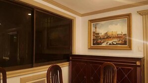 A room with a large window, a painting of a historical building, and a wooden cabinet with chairs. - Elegant 2BRCondo in the Heart of Ortigas (Pasig)