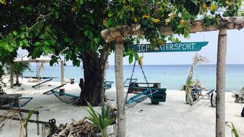 A beach area with hammocks, a sign reading "ICP Watersport", and a view of the ocean.