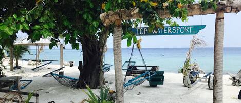 A beach area with hammocks, a sign reading "ICP Watersport", and a view of the ocean.