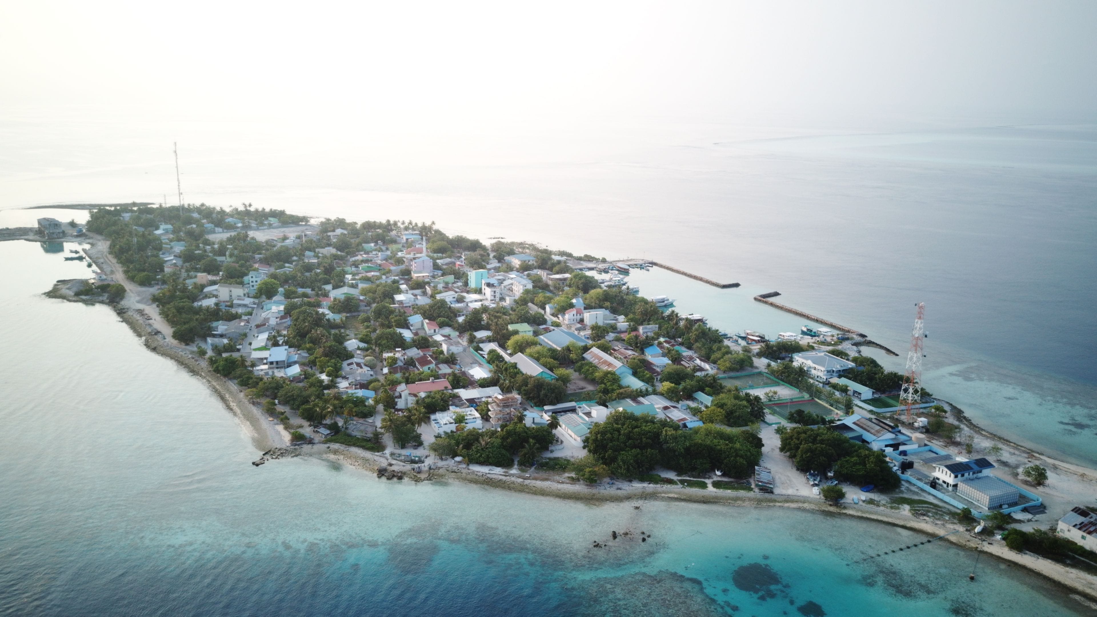 An aerial view of a coastal town with buildings, a pier, and clear blue waters.