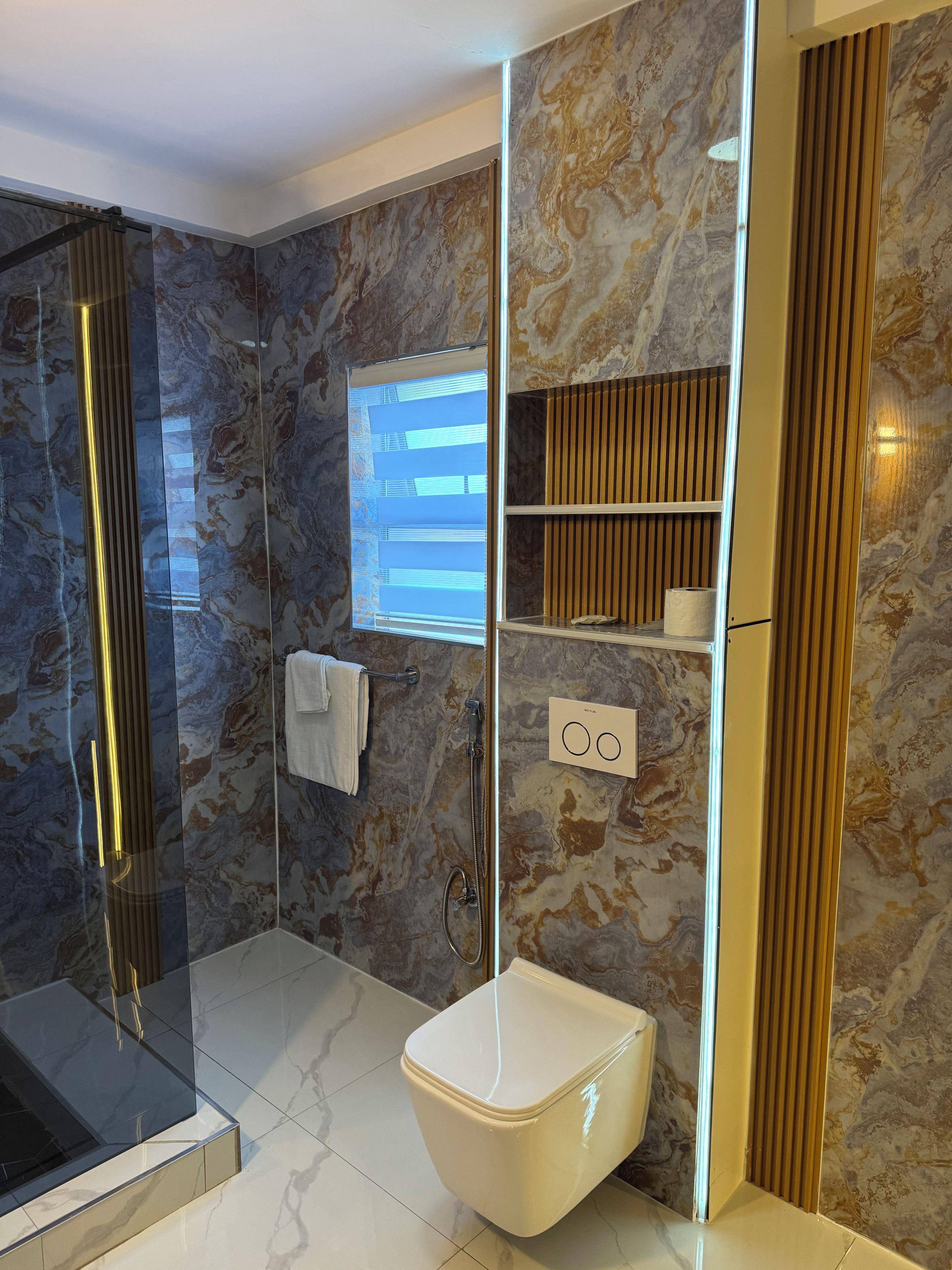 A modern bathroom with a glass-enclosed shower, a toilet, and marble-patterned walls.