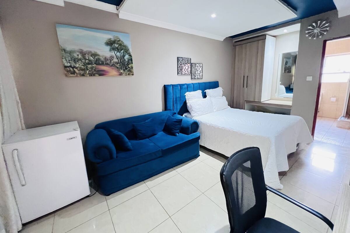 A bedroom with a bed, a blue sofa, a white refrigerator, and a chair.