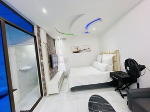 Una habitación de hotel moderna con cama, escritorio, silla, ventilador y televisión.