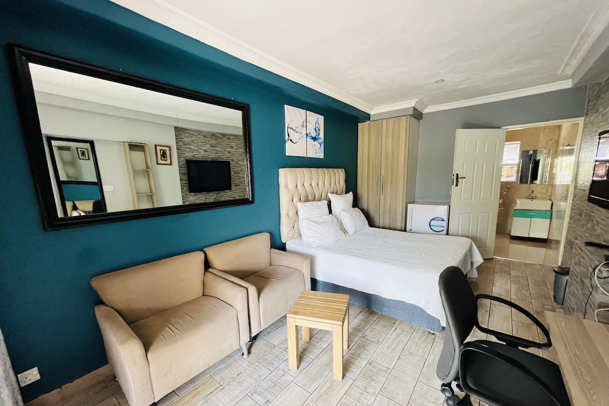 A hotel room with a bed, a sofa, a small table, a chair, a mirror, and a wardrobe.