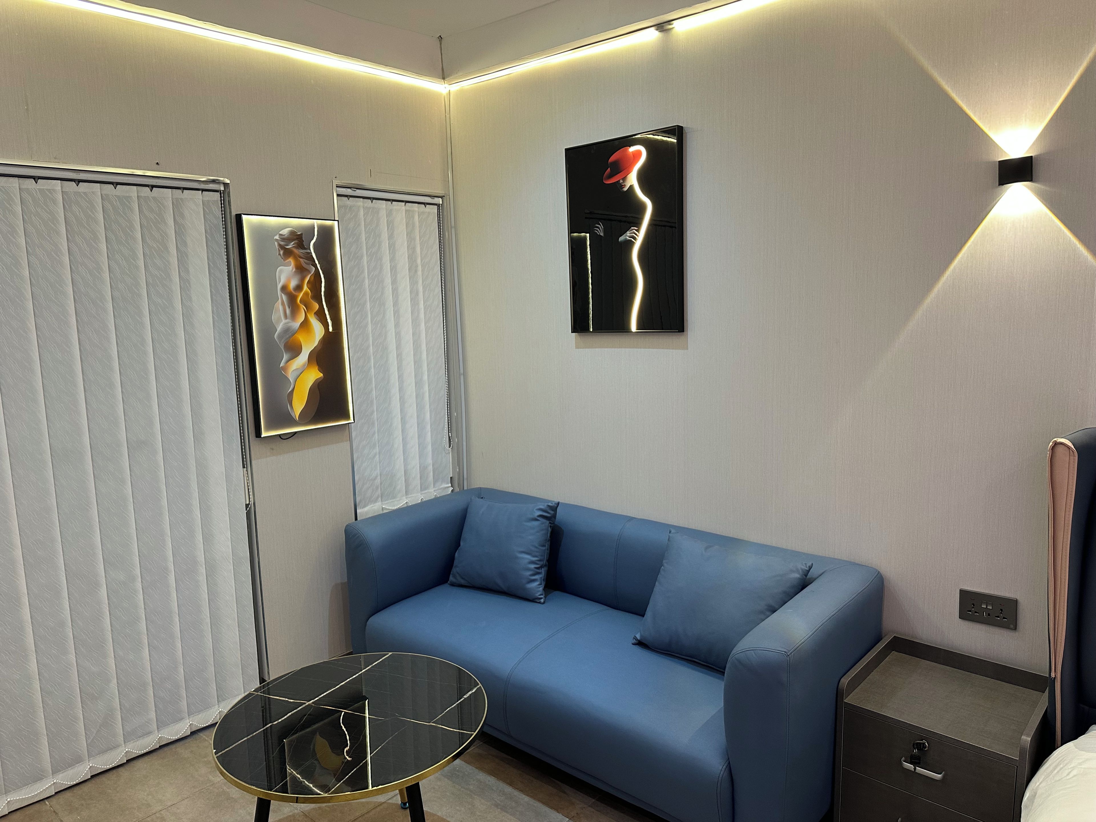 Een moderne kamer met een blauwe bank, een tafel met glazen blad en kunstwerken aan de wanden.