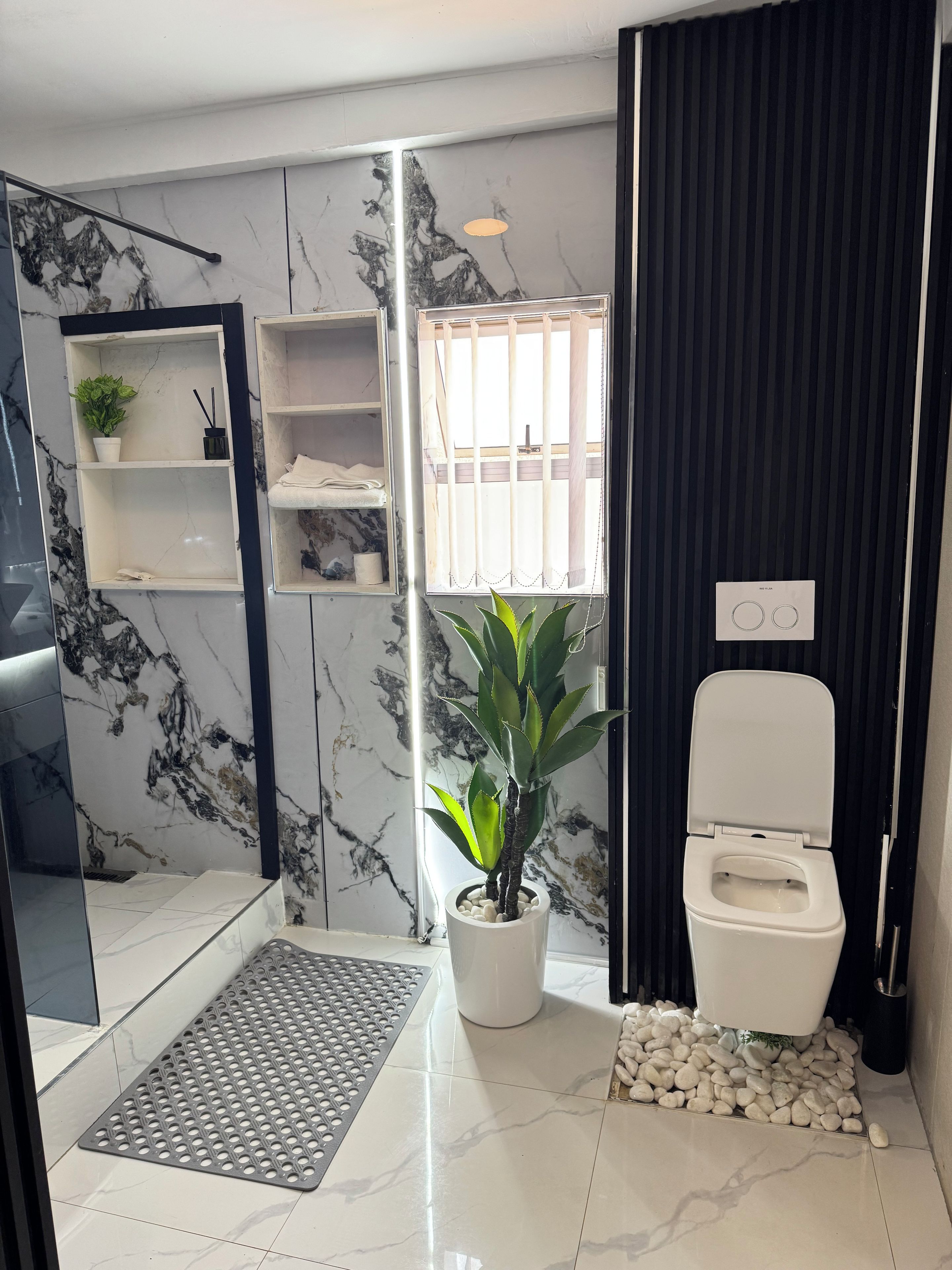 Une salle de bain moderne avec douche, toilettes, murs en marbre et une plante en pot.