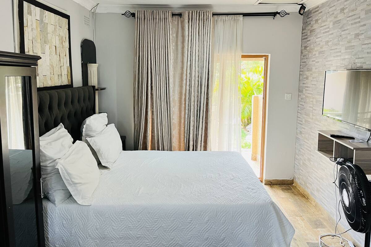 A bedroom with a bed, a TV, and a fan.