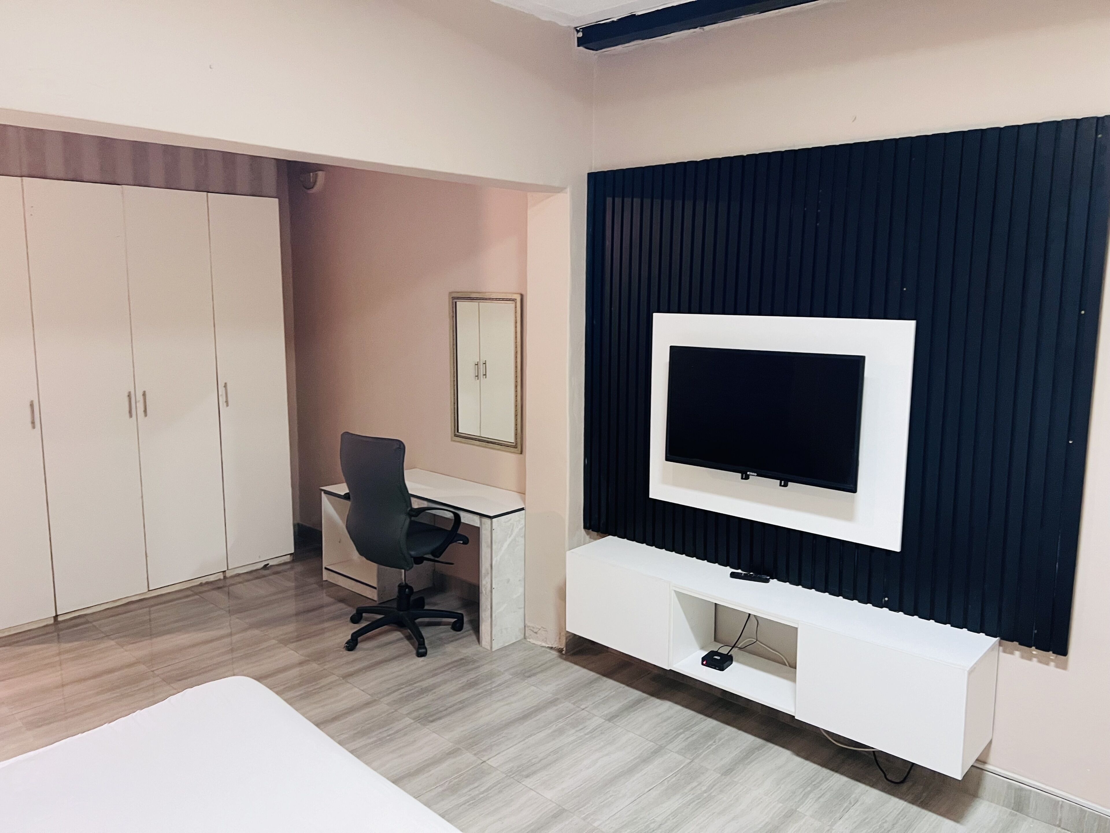 A room with a desk, office chair, wardrobe, and a mounted TV on a wall.