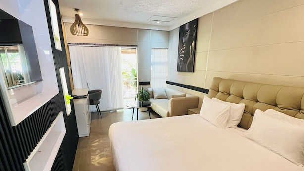 A hotel room with a large bed, a desk, a chair, a sofa, and a dining table. - Highlands Lodges and Apartments (Harare)