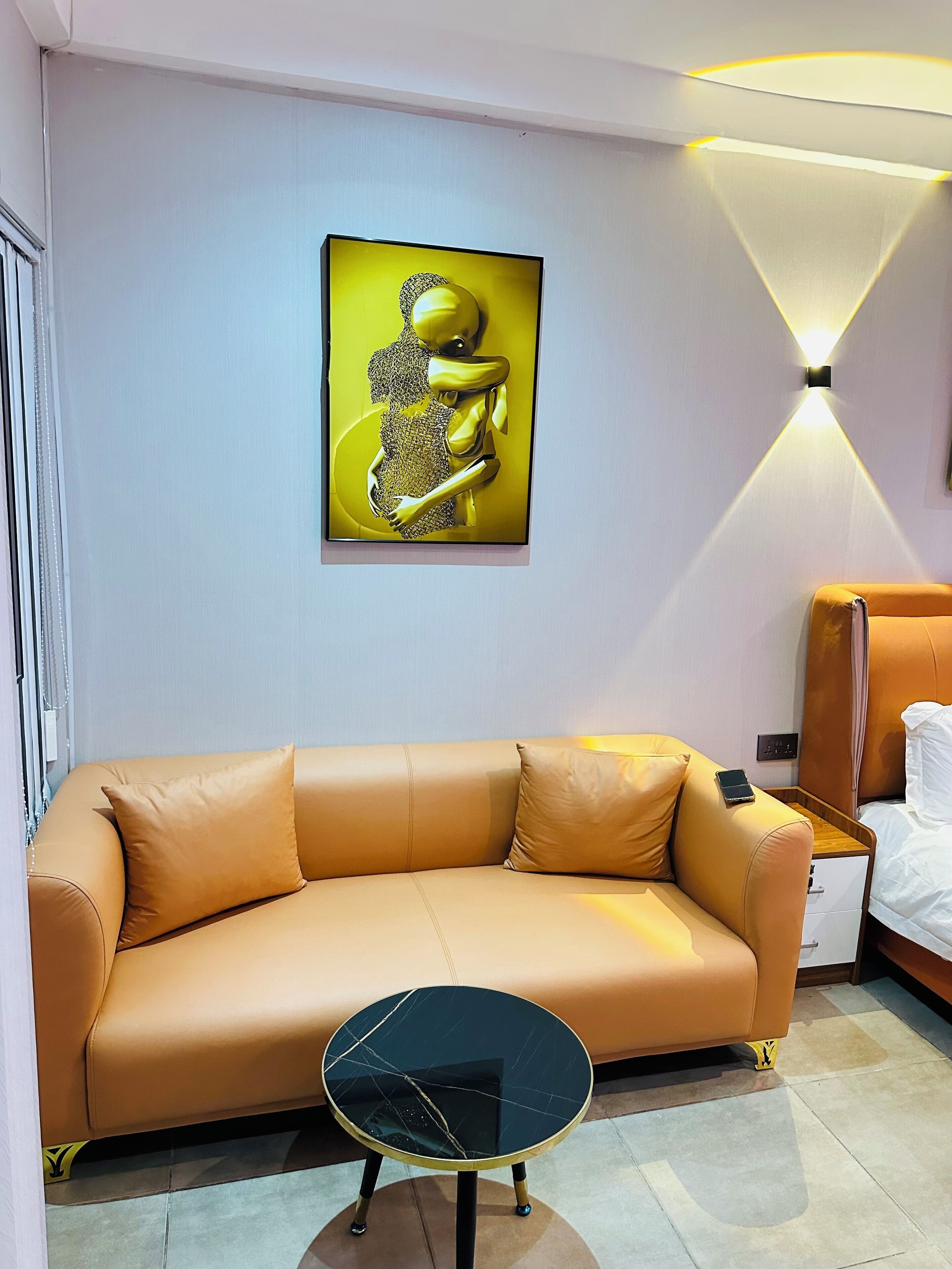 A modern room with a tan leather sofa, a small black marble table, and a wall-mounted artwork.