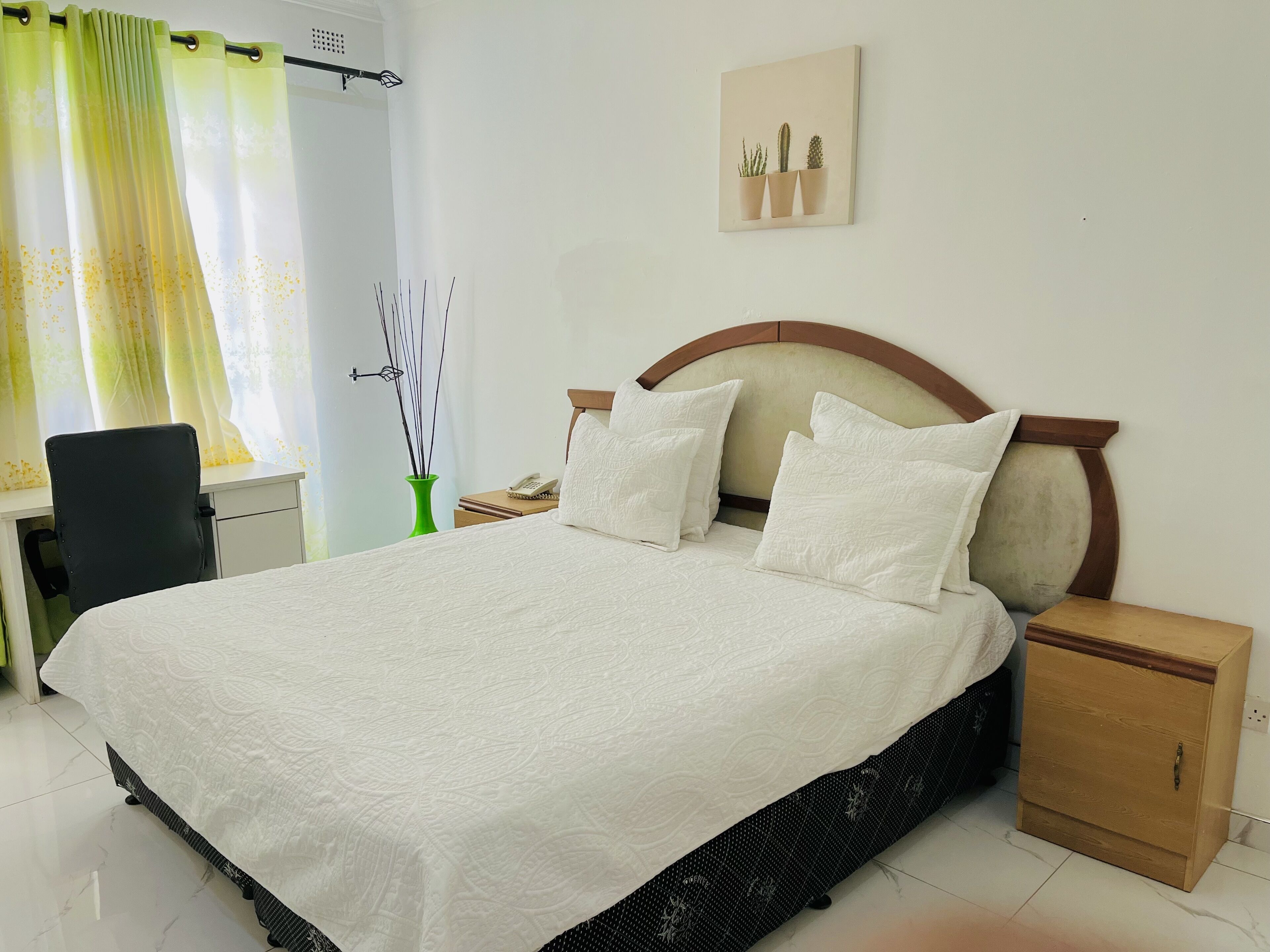 A neatly made bed with a white bedspread, a wooden headboard, and two bedside tables with lamps.