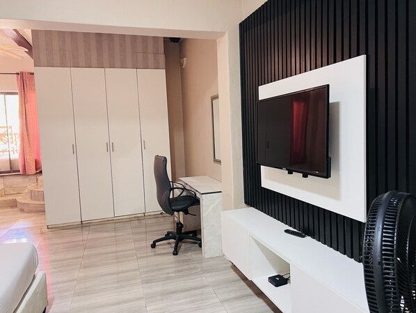 A modern room with a TV mounted on a black wall, a white desk, and a black office chair.