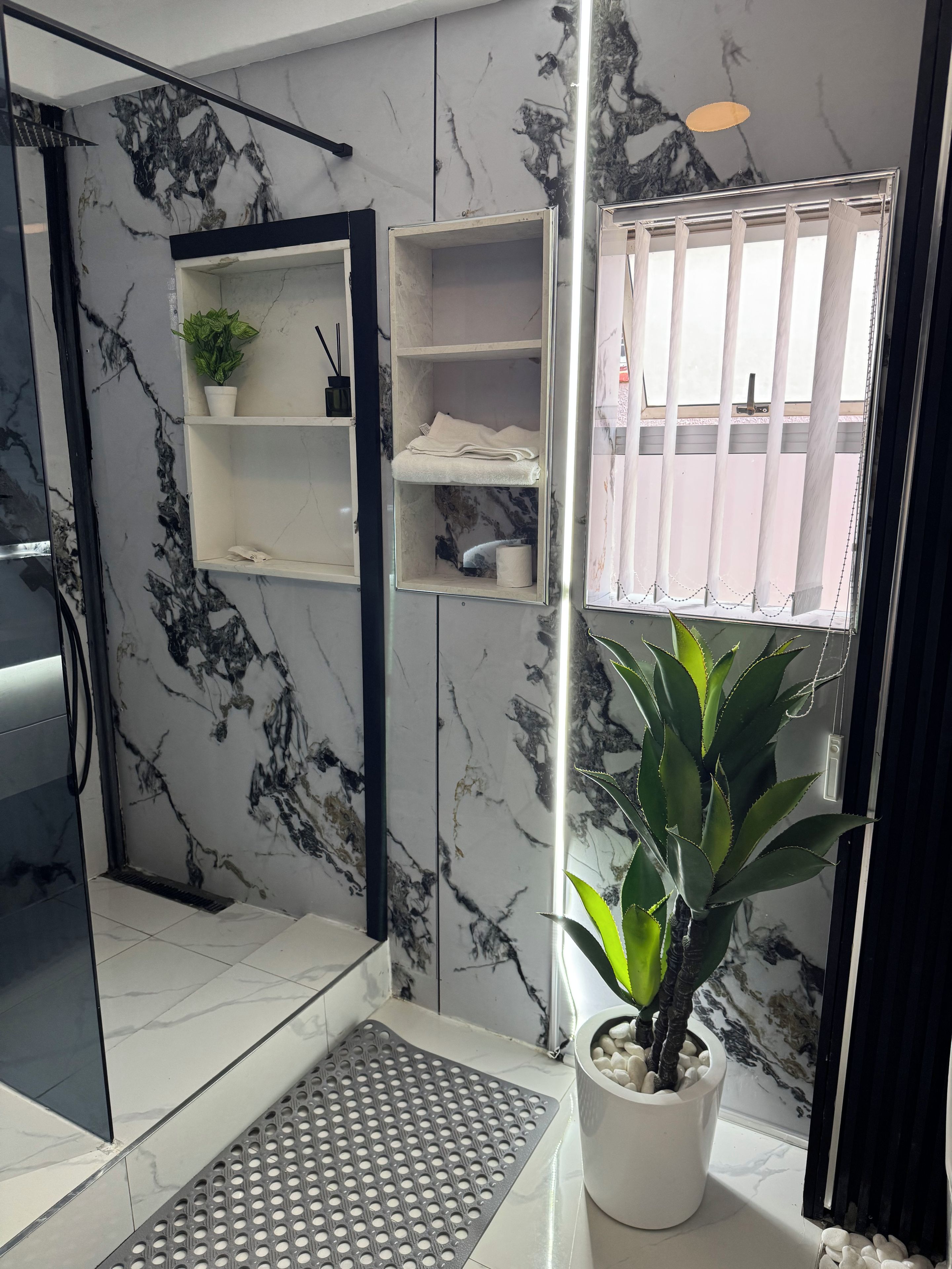 A bathroom with a marble wall, a shower area, a sink, a toilet, and a window with a view.
