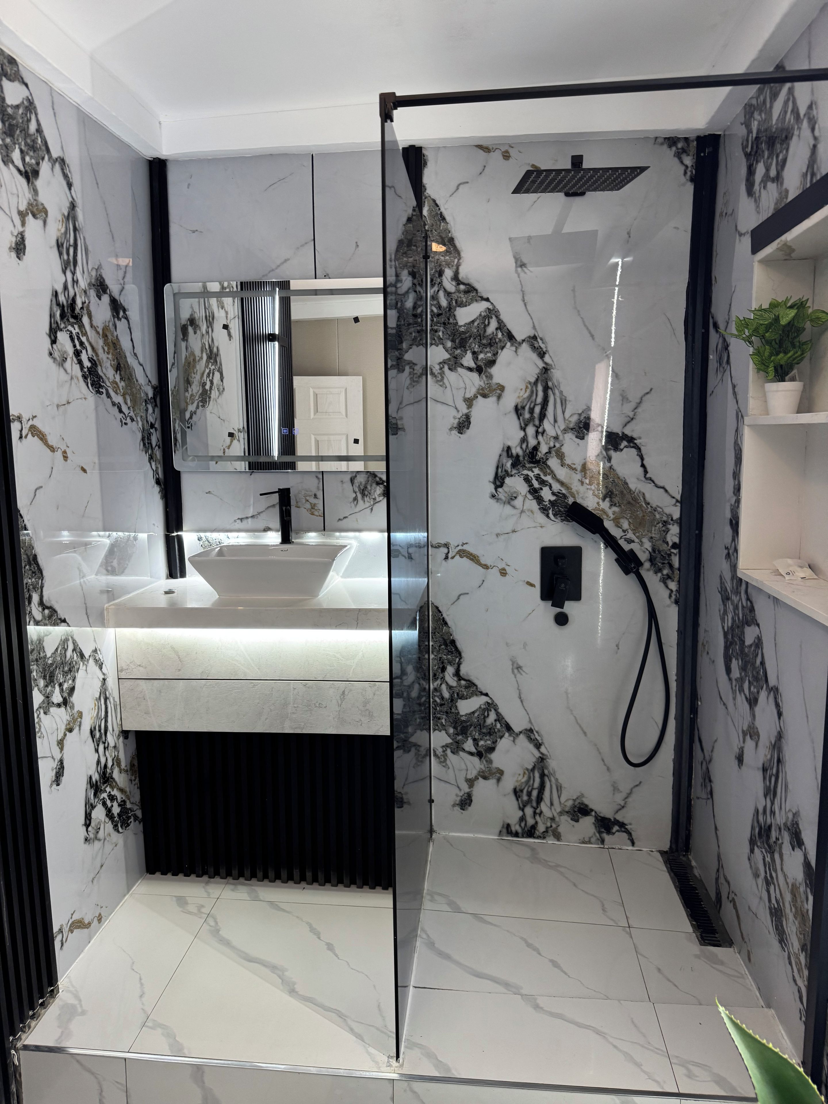A modern bathroom with a glass-enclosed shower, a white marble sink, and a black-framed mirror.