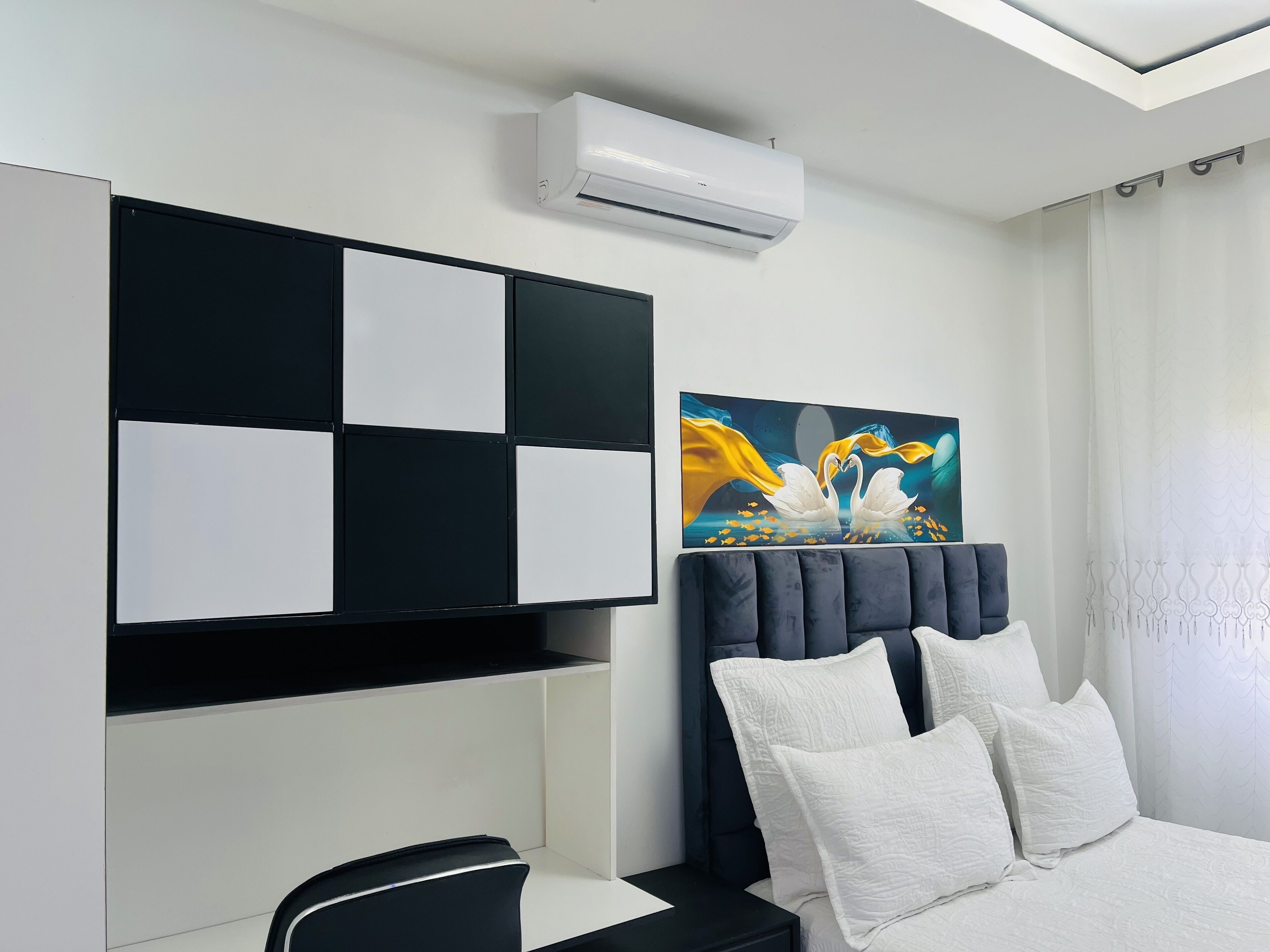 Una camera da letto moderna con un letto, un armadietto bianco e nero, un quadro e un condizionatore d'aria.
