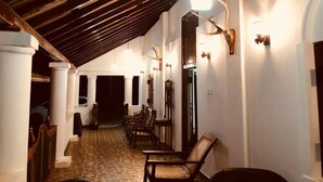 A corridor with a tiled floor, wooden beams, white pillars, and wall-mounted light fixtures.