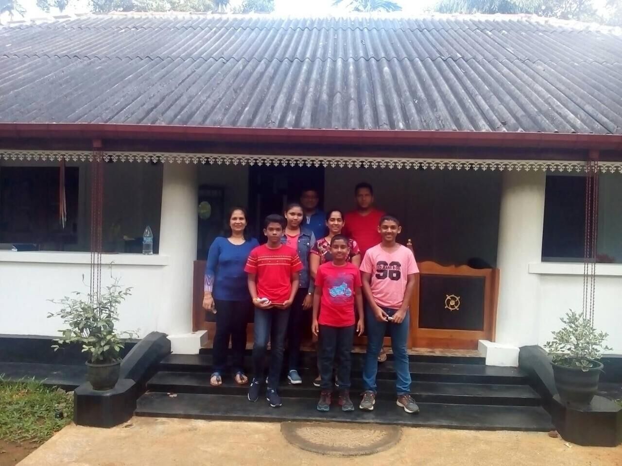 A group of people standing in front of a building with a tiled roof and a porch.