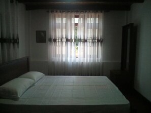 A bedroom with a bed, curtains, a window, and a mirror.