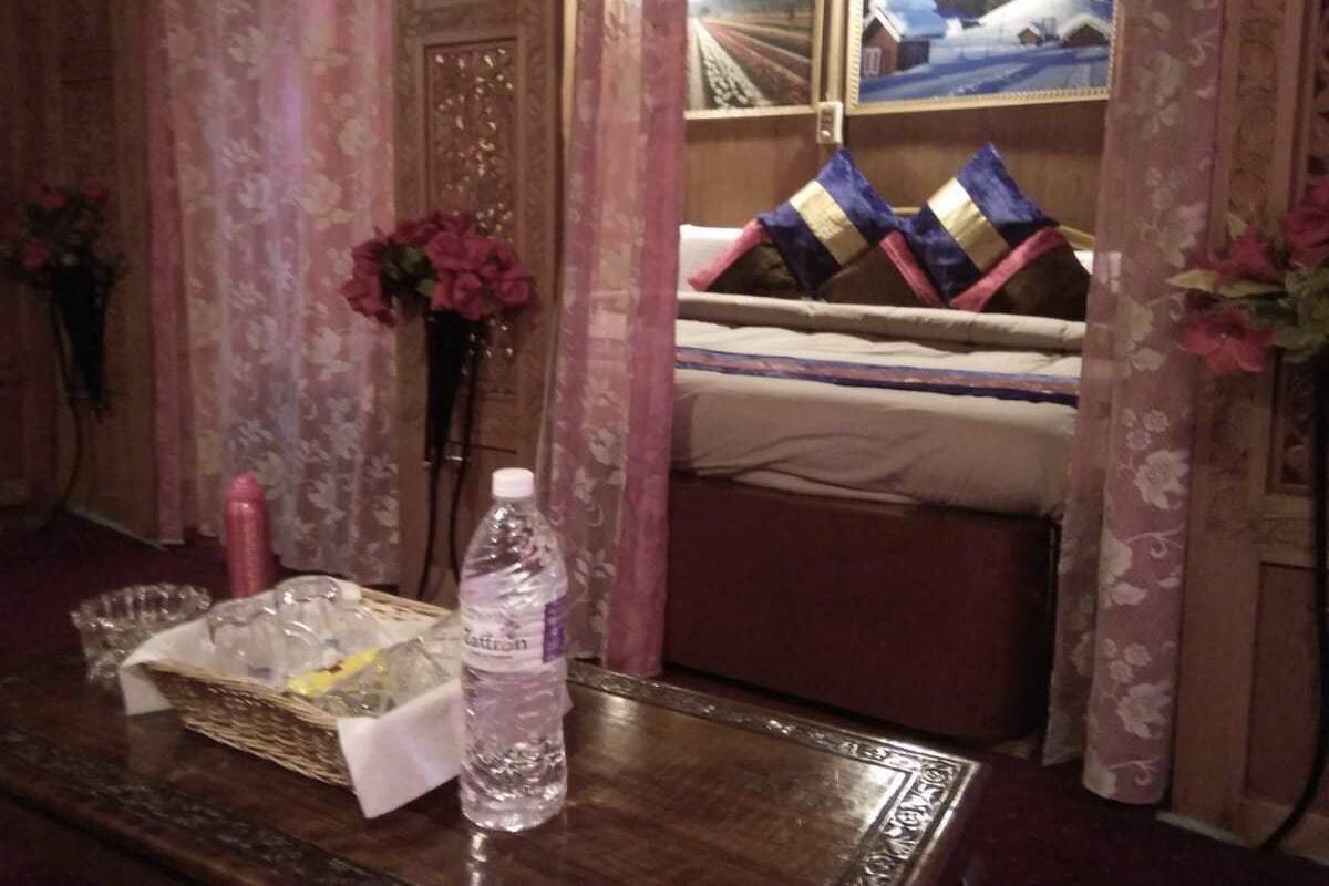 A hotel room with a bed, a bedside table with a water bottle, a basket, and a vase with flowers.