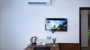 A room with a mounted TV, a table with a kettle, plates, glasses, and a vase with flowers. - Hotel Royal Suite (Kathmandu)