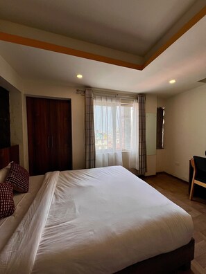 A hotel room with a large bed, a wardrobe, a desk, and a window with curtains.