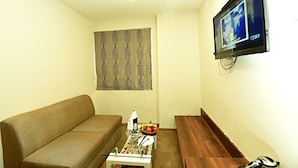 A living room with a brown sofa, a coffee table with magazines and a bottle, a TV on the wall, and a patterned curtain. - Hotel Royal Suite (Kathmandu)