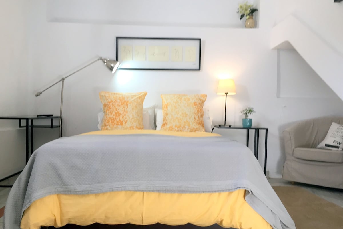 A neatly arranged bedroom with a bed, two bedside tables, a lamp, a framed picture on the wall, and a small plant.