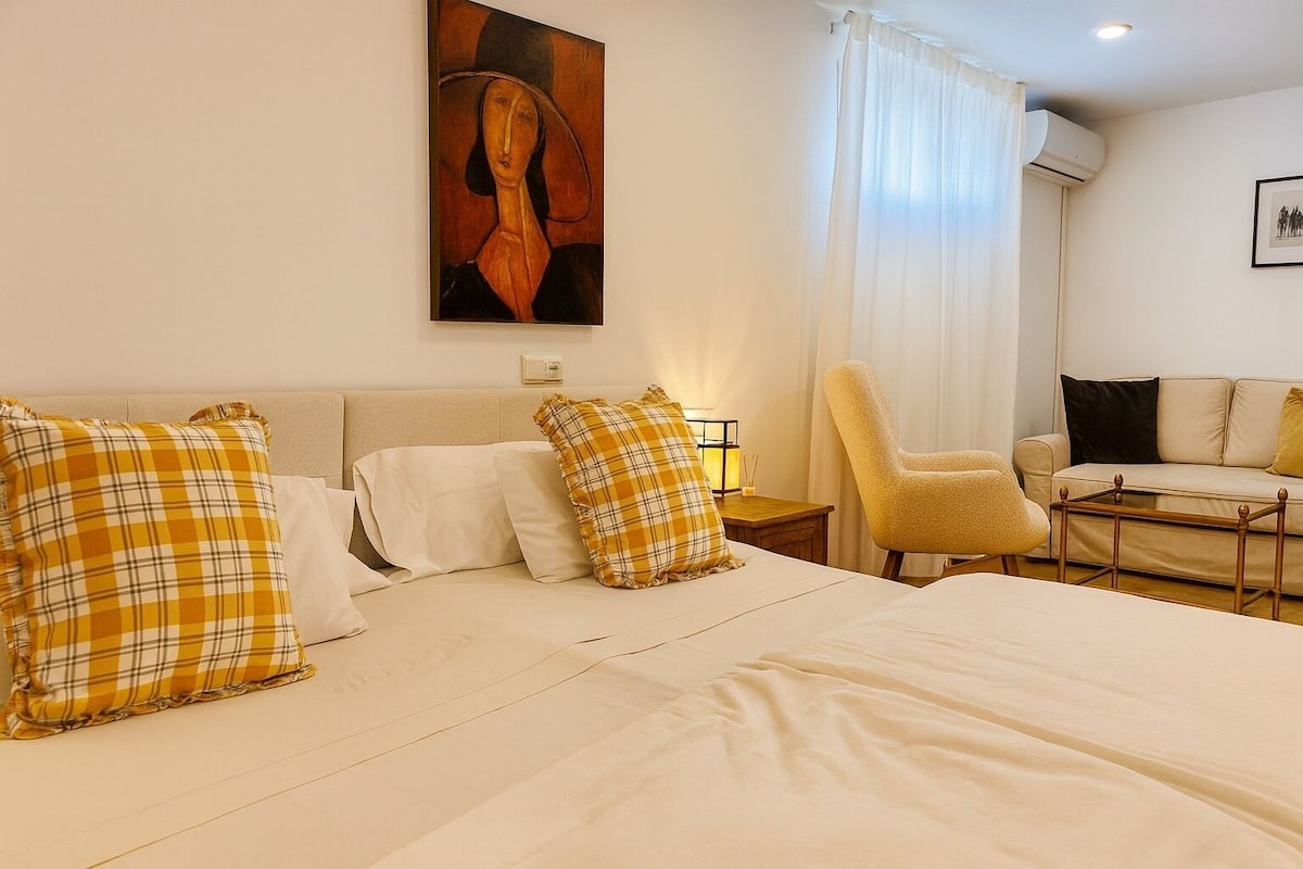 A hotel room with a large bed, a chair, a sofa, and a painting on the wall.