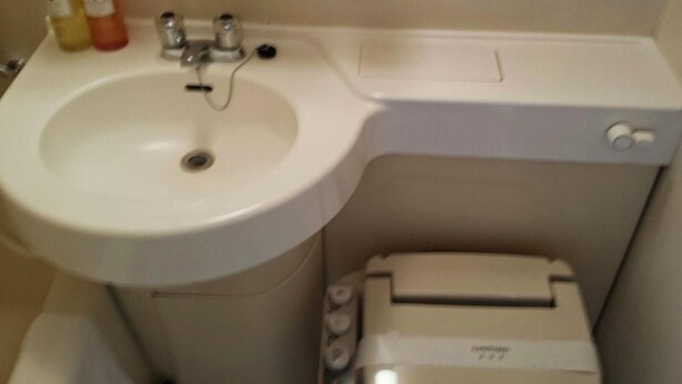 A bathroom with a white sink, a toilet, and a trash bin. - Uwajima Regent Hotel (Uwajima)