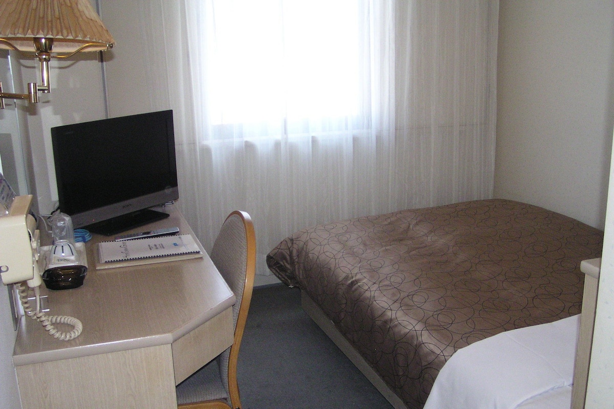 Habitación de hotel con escritorio, computadora, lámpara, teléfono y cama con colcha estampada.
