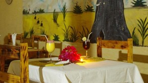 A dining table with a white tablecloth, two drinks, and a floral centerpiece. - Hotel Mimosa - Hostel (Toubab Dialao)