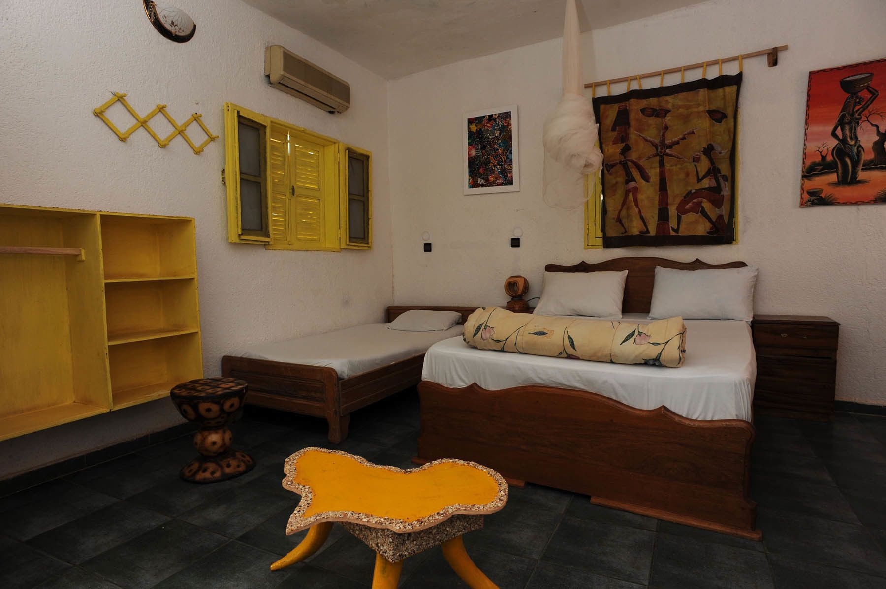 Un dormitorio con dos camas individuales, un armario de madera, un taburete pequeño y un aire acondicionado de pared.