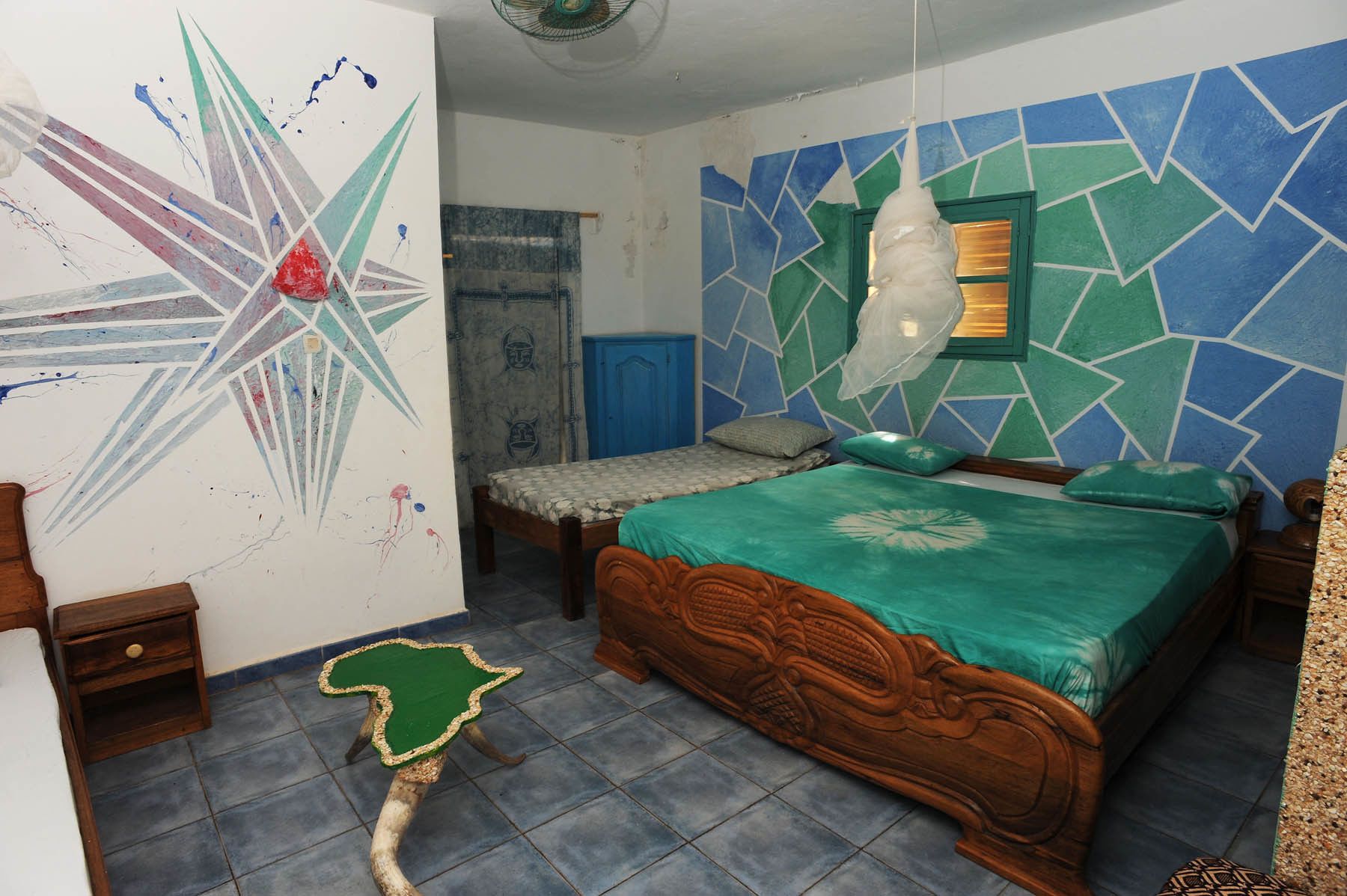 A bedroom with a bed, a nightstand, a wall with a geometric pattern, and a ceiling fan.