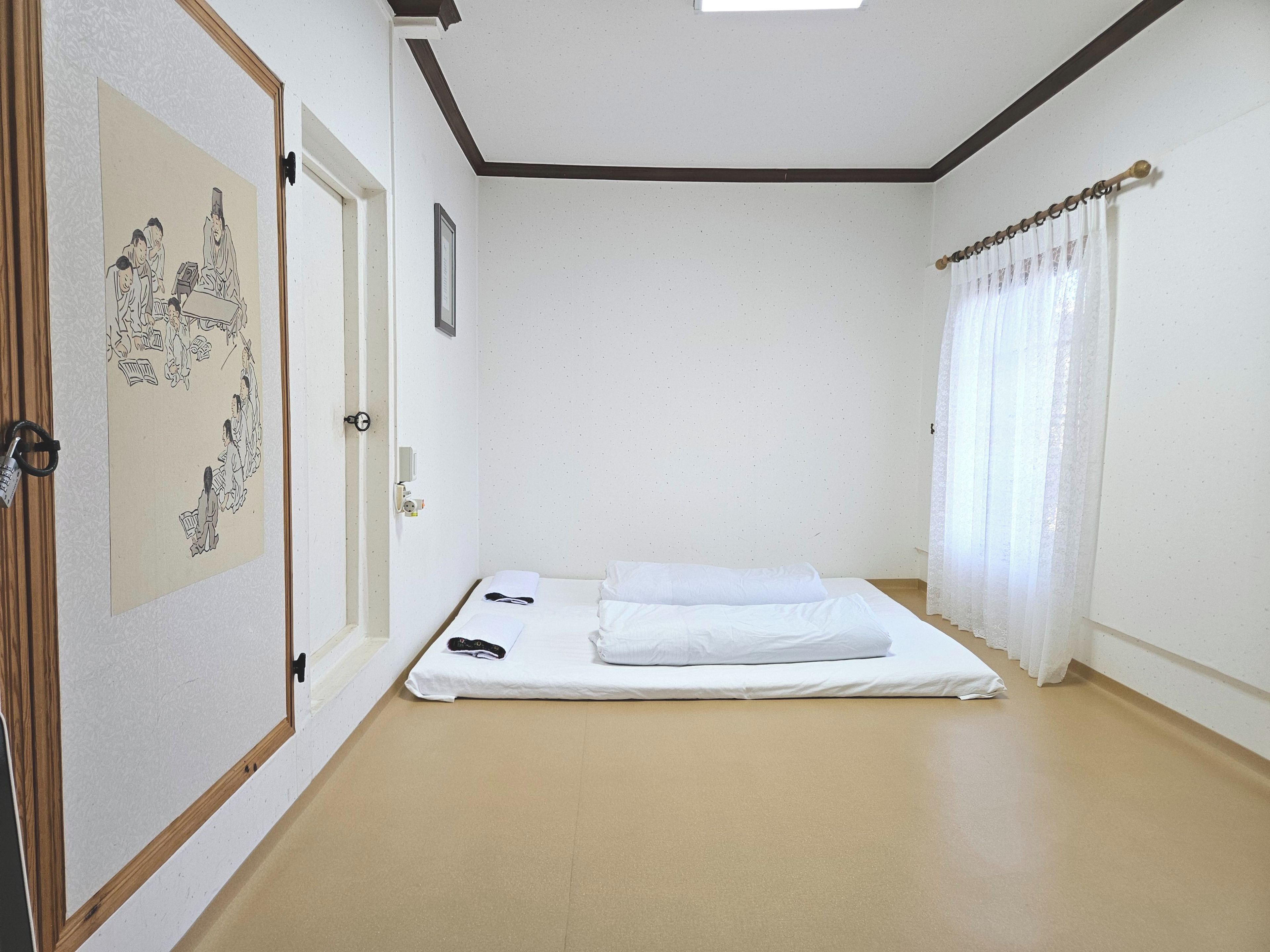 Une chambre avec un lit simple, une porte ornée d’un tableau traditionnel et un rideau.