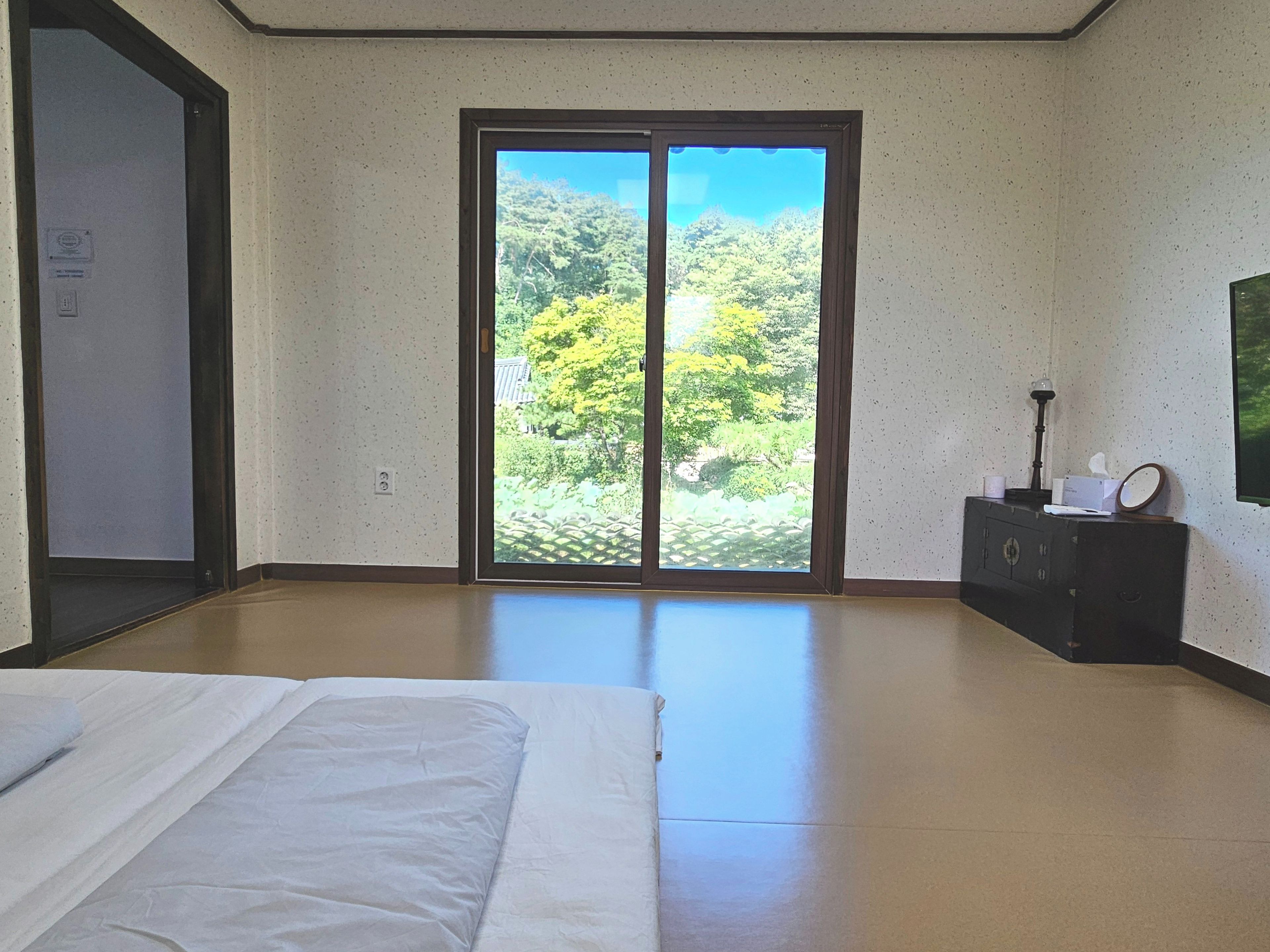A hotel room with a bed, a dresser, and a view of greenery through a sliding door.