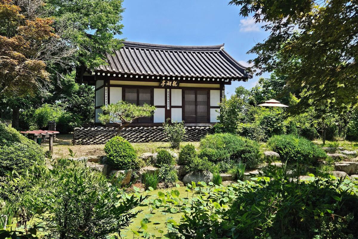 A traditional Japanese building with a tiled roof, surrounded by lush greenery and a pond.