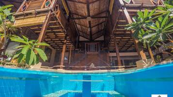 A view of a poolside area with a wooden deck, palm trees, and a clear blue pool.