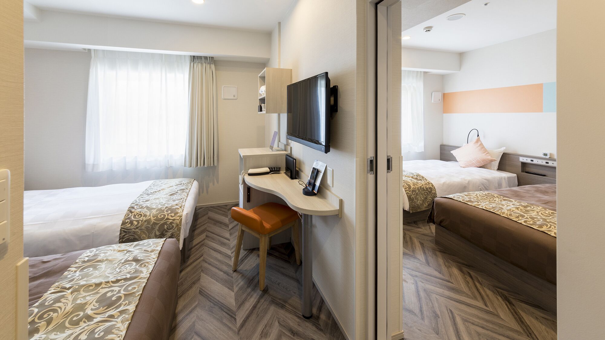 A hotel room with two beds, a desk with a chair, a television, and a wardrobe.