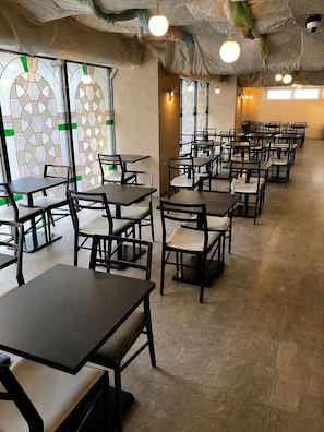 A restaurant interior with multiple tables and chairs, patterned windows, and hanging light fixtures. - SARASA HOTEL Shin-Osaka (Osaka)