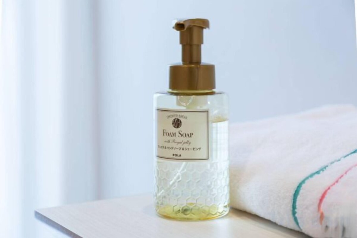 A bottle of foam soap on a white surface with a towel in the background.