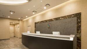 A modern hotel reception area with a curved reception desk, marble flooring, and a large wall-mounted logo. - SARASA HOTEL Shin-Osaka (Osaka)