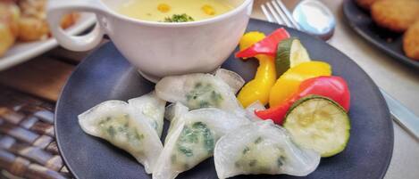 Um prato de dumplings, uma tigela de sopa e legumes fatiados.